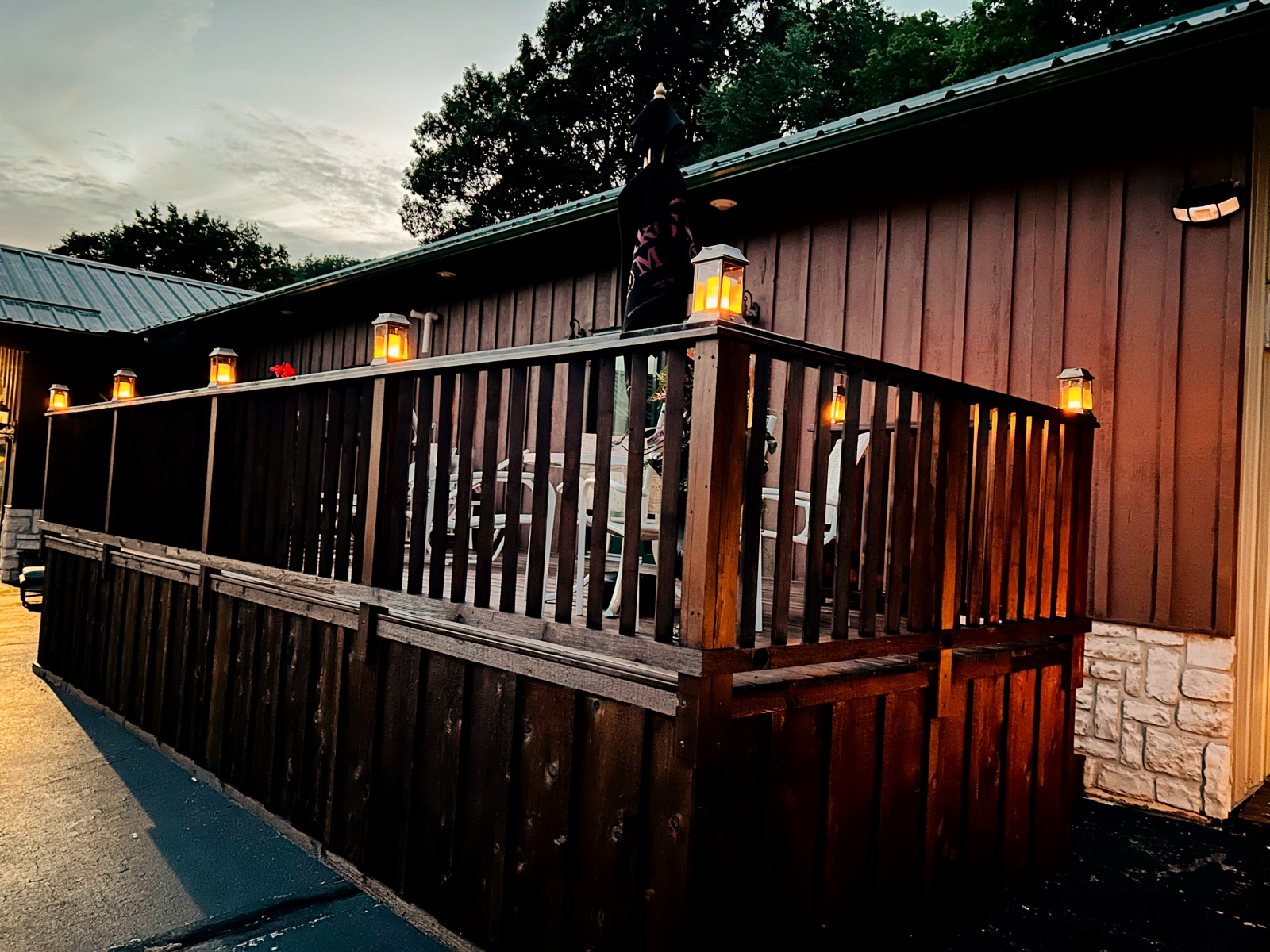The deck at dusk — lanterns lit along the rail, the last light behind the trees