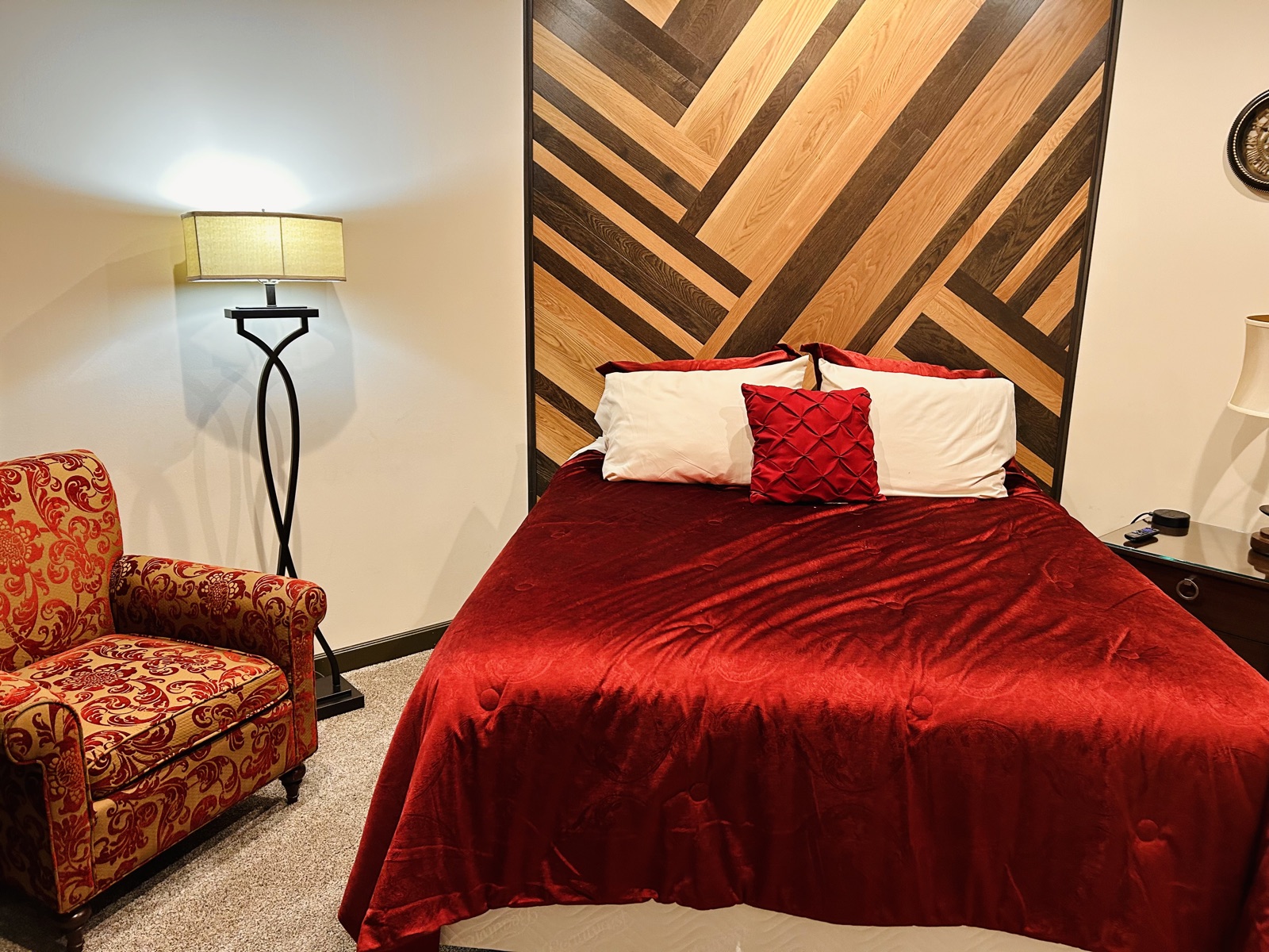 A king bed under a floor-to-ceiling headboard of herringbone wood planks, red bedding below