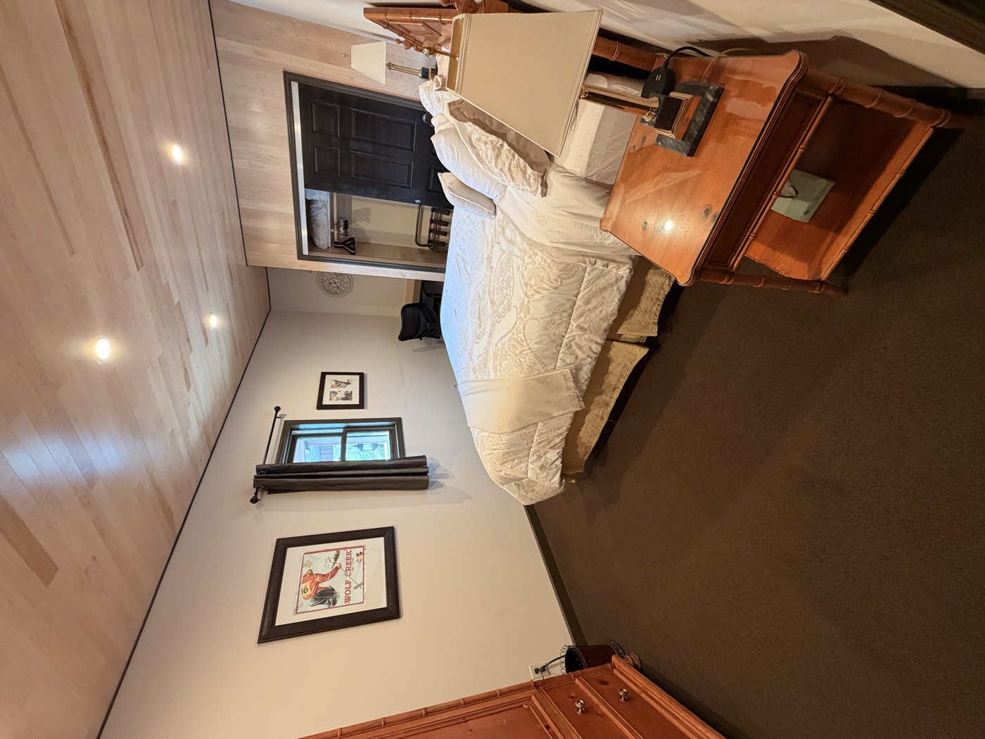 A bedroom under the plank ceiling — white bedding, a bedside lamp, the closet beyond