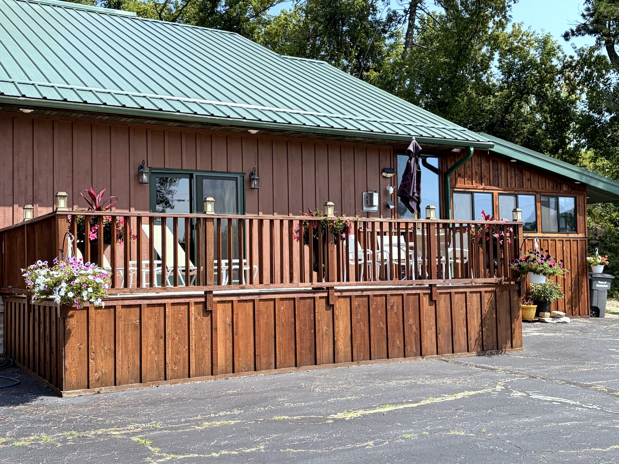 The deck along the front of the house: flower baskets on the rail, the green metal roof above, the drive in front