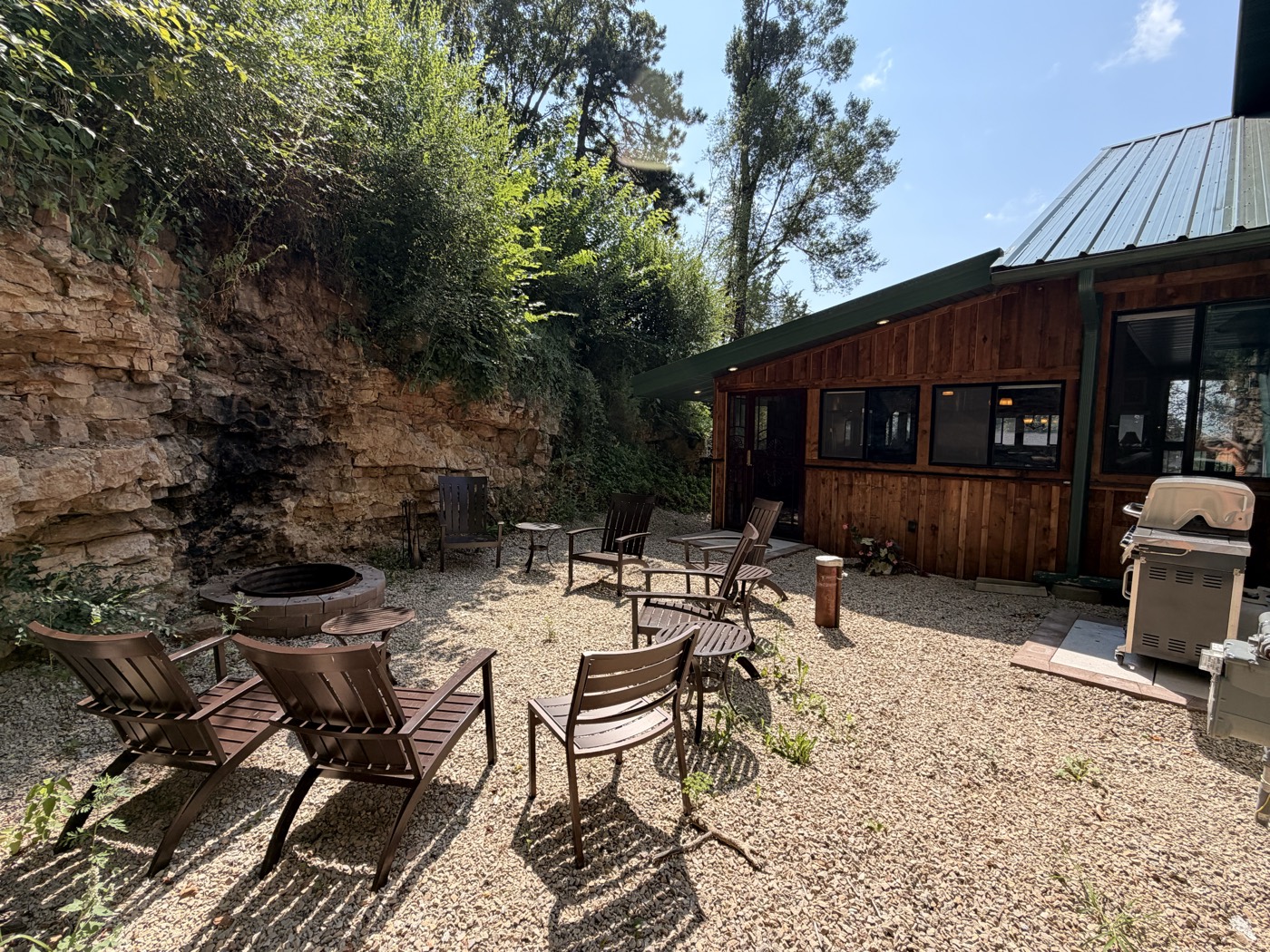 An outdoor fire pit with chairs around it, against a rock bluff