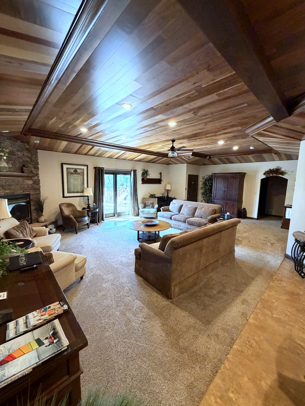 The great room from the doorway: the plank ceiling, the stone fireplace, the sofas and the patio door beyond