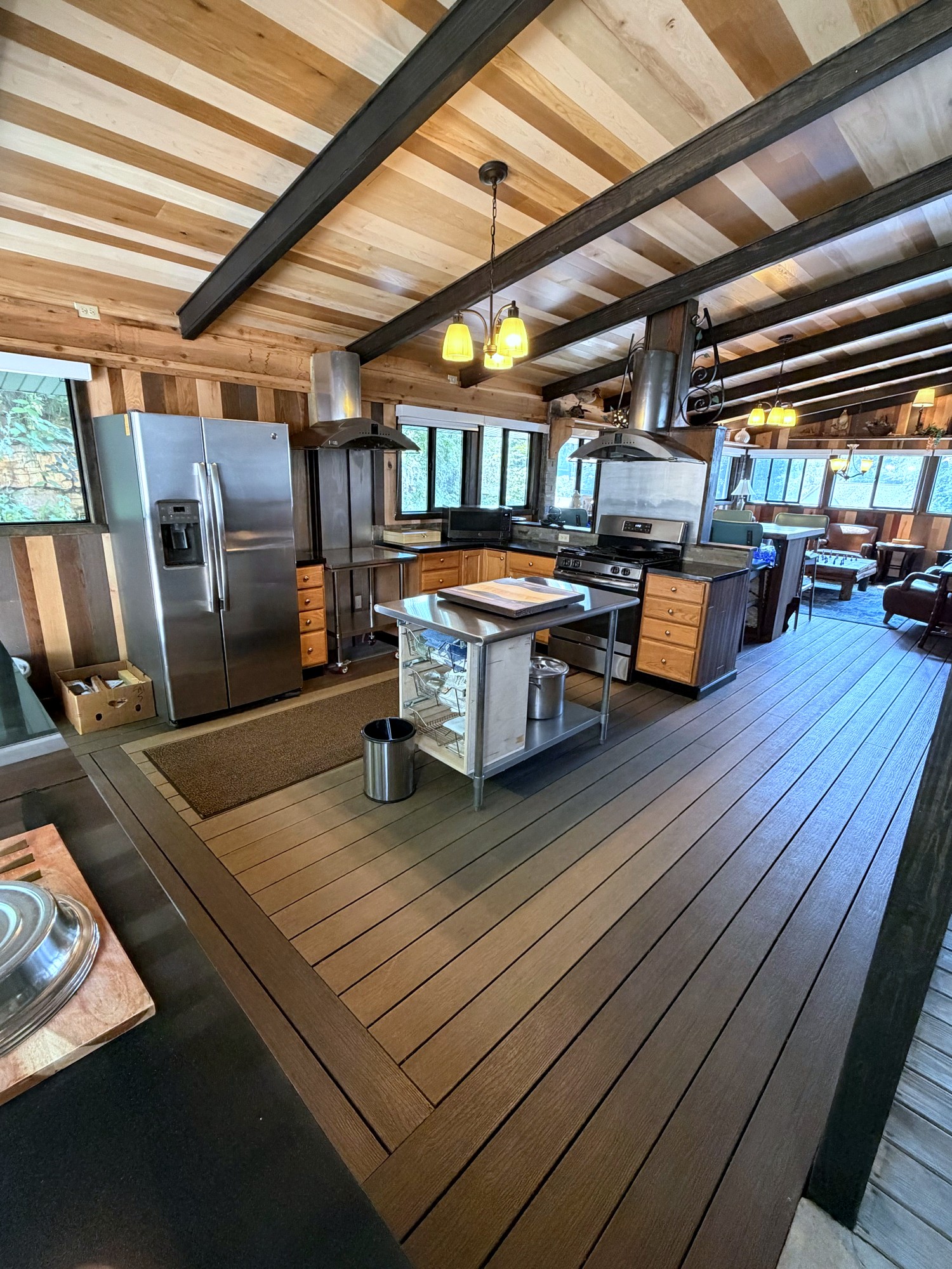 The three-season room: the summer kitchen with its stainless refrigerator and range, an island, and seating beyond, under exposed beams
